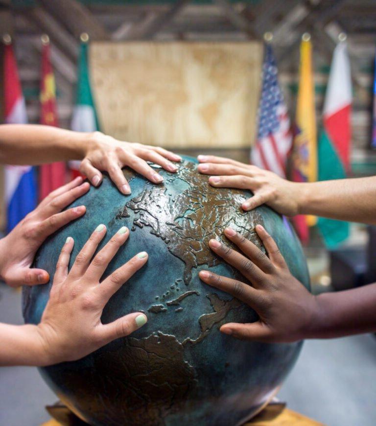 students place thier hands together on a globe